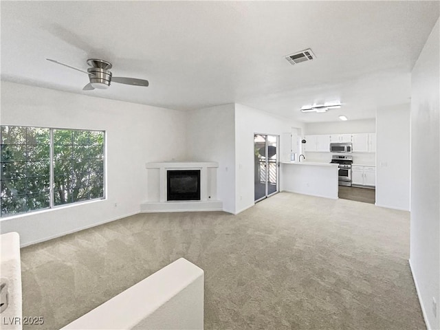 unfurnished living room featuring visible vents, a glass covered fireplace, carpet flooring, ceiling fan, and baseboards