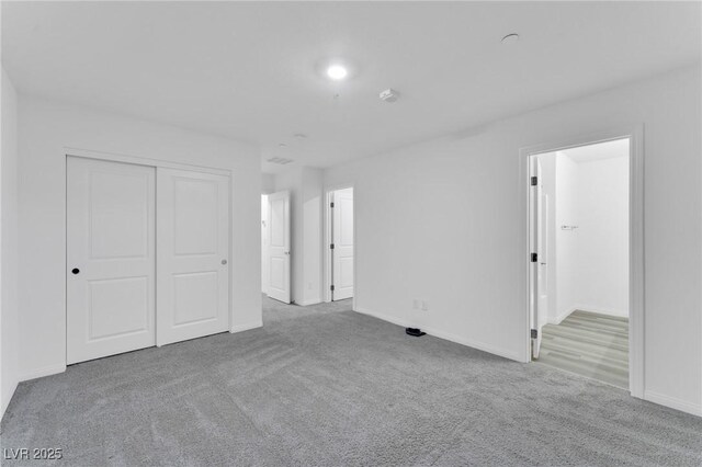 unfurnished bedroom featuring a closet, light carpet, baseboards, and ensuite bath