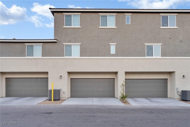 back of property featuring driveway, central AC unit, an attached garage, and stucco siding