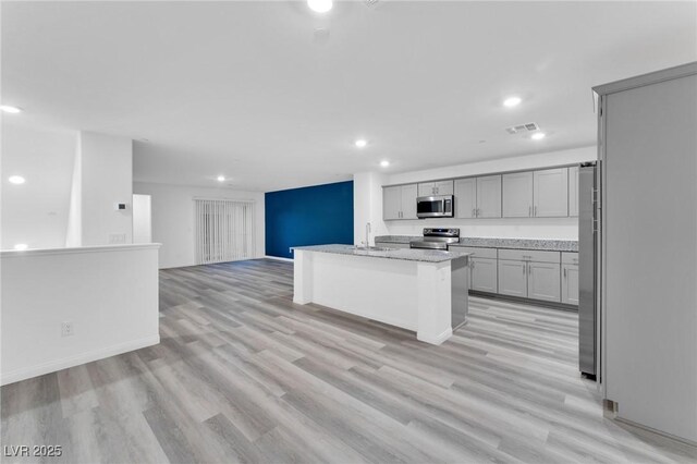 kitchen with a sink, visible vents, open floor plan, appliances with stainless steel finishes, and an island with sink