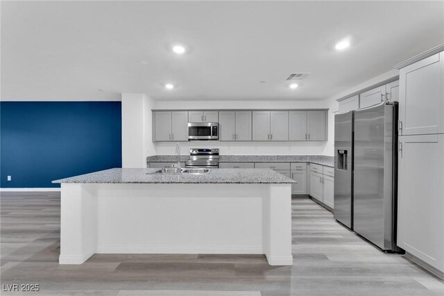 kitchen featuring light stone counters, a sink, visible vents, appliances with stainless steel finishes, and a center island with sink