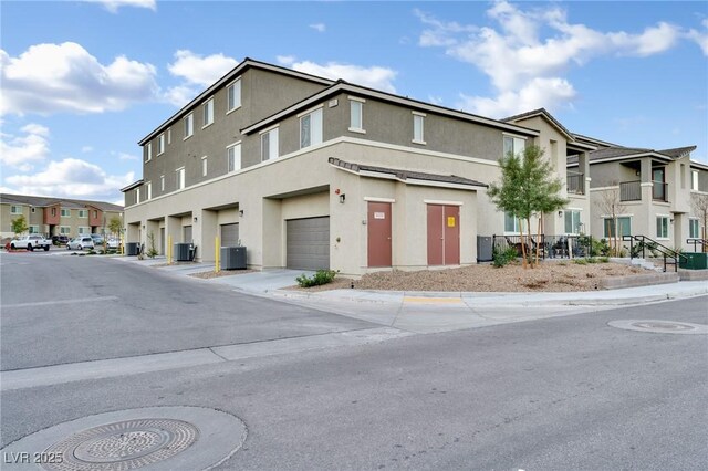 view of front of home featuring a garage, a residential view, stucco siding, and central AC unit