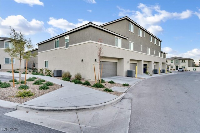 view of front of property featuring an attached garage, a residential view, central AC unit, and stucco siding