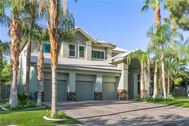 mediterranean / spanish home featuring an attached garage, a tile roof, stone siding, decorative driveway, and stucco siding