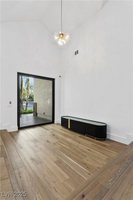 unfurnished room with a notable chandelier, a towering ceiling, baseboards, and wood finished floors