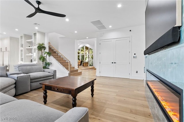 living area featuring stairway, visible vents, light wood-style flooring, and a tiled fireplace