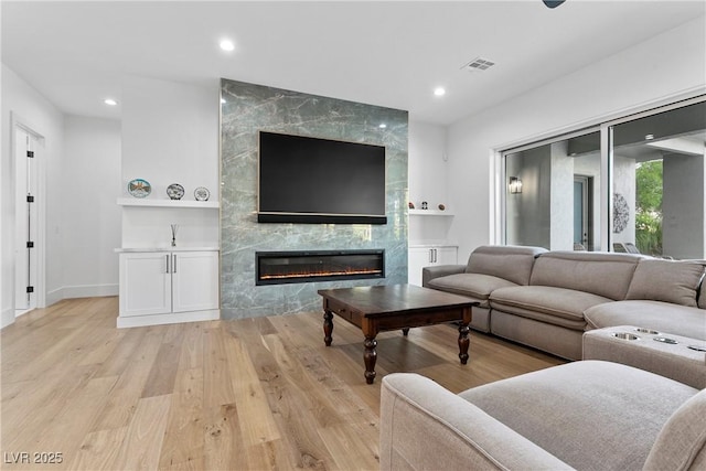 living room with a fireplace, light wood finished floors, recessed lighting, visible vents, and baseboards