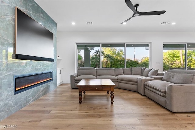 living room with light wood finished floors, a tiled fireplace, visible vents, and recessed lighting