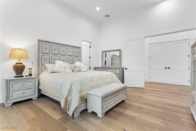 bedroom with light wood finished floors, a high ceiling, visible vents, and recessed lighting