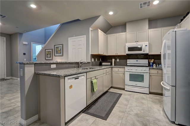 kitchen featuring light stone counters, a peninsula, white appliances, a sink, and visible vents