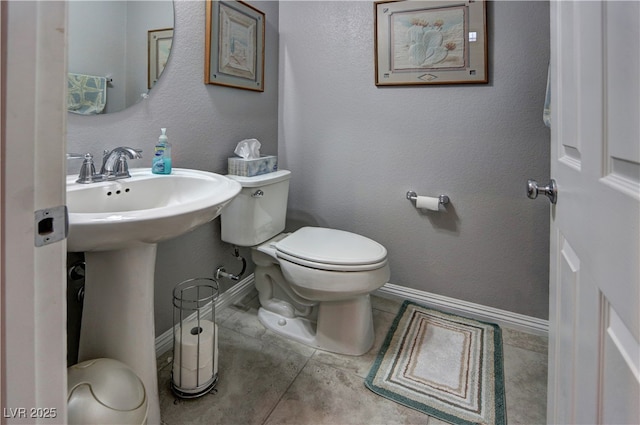 bathroom with a textured wall, toilet, a sink, baseboards, and tile patterned floors