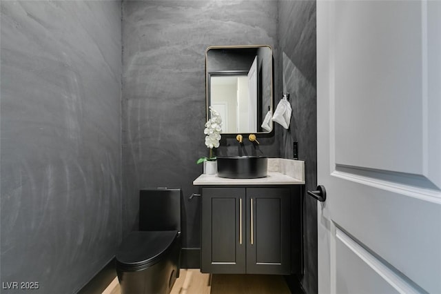 half bath with toilet, wood finished floors, and vanity