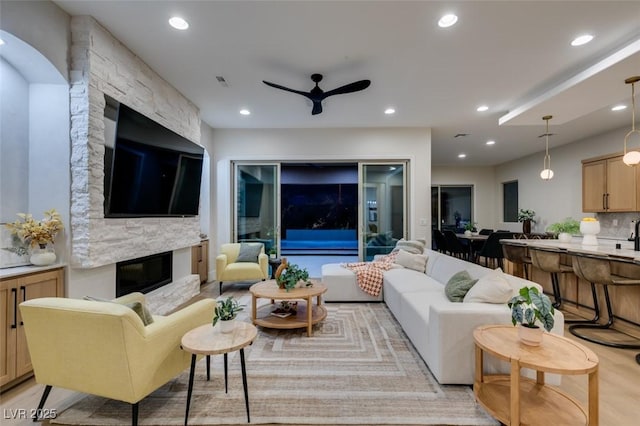 living area featuring visible vents, a ceiling fan, light wood-style flooring, a stone fireplace, and recessed lighting