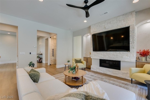 living room featuring ceiling fan, light wood-style flooring, a fireplace, visible vents, and baseboards