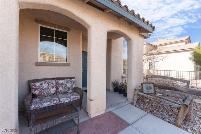 view of exterior entry featuring a tiled roof, fence, and stucco siding