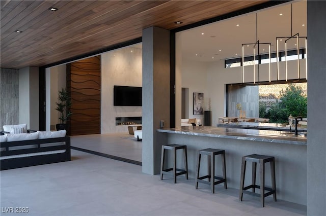 interior space with wood ceiling, modern cabinets, light stone counters, open floor plan, and a kitchen bar