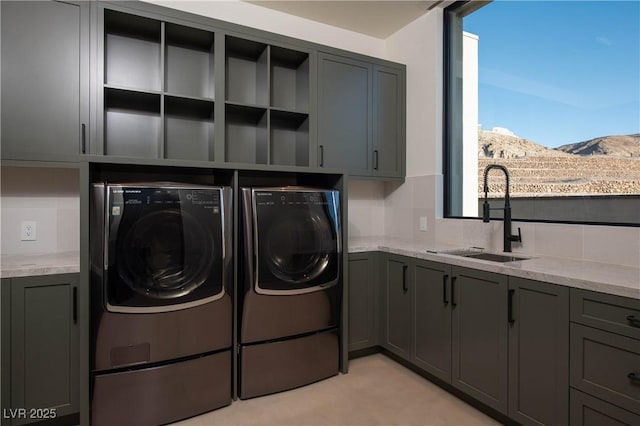 clothes washing area featuring cabinet space, washing machine and dryer, a mountain view, and a sink