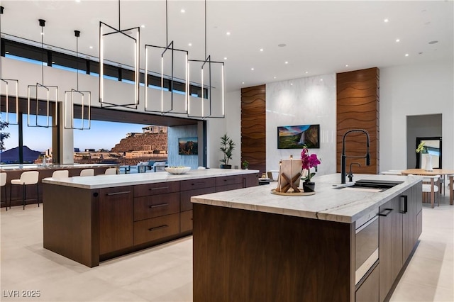 kitchen with modern cabinets, a large island with sink, a sink, and dark brown cabinets
