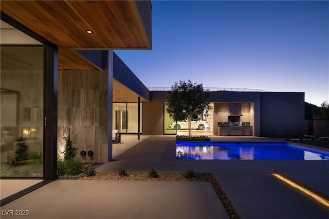 pool at dusk featuring an outdoor pool, exterior kitchen, and a patio