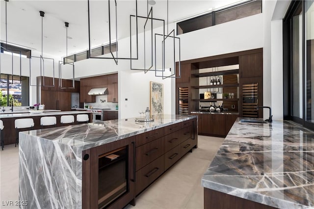 kitchen with extractor fan, a large island with sink, stone counters, pendant lighting, and a sink