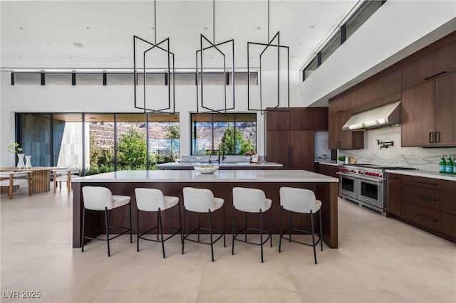 kitchen featuring a breakfast bar area, light countertops, wall chimney range hood, modern cabinets, and double oven range