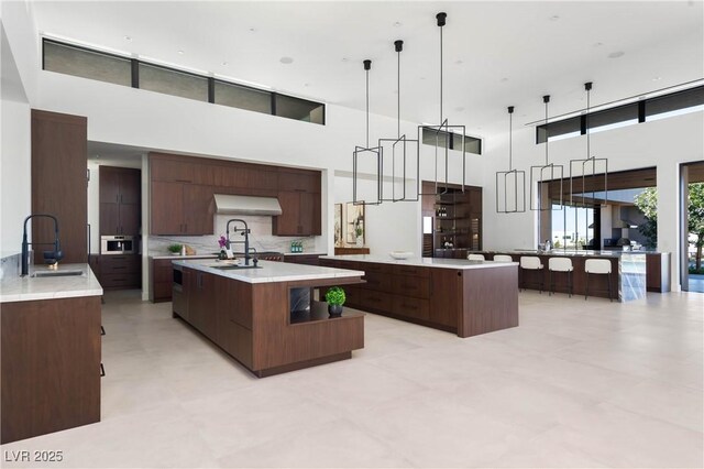 kitchen with modern cabinets, a large island with sink, decorative backsplash, and a sink