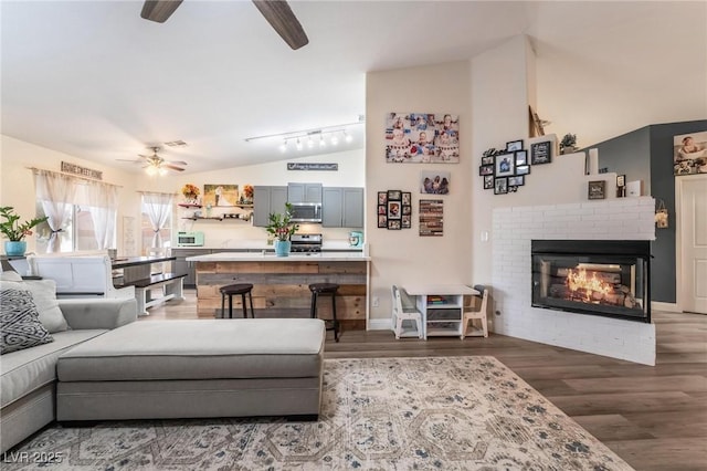 living area with wood finished floors, lofted ceiling, ceiling fan, track lighting, and a brick fireplace