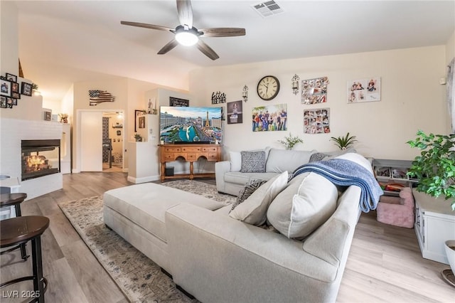 living room with visible vents, a multi sided fireplace, light wood-type flooring, lofted ceiling, and a ceiling fan