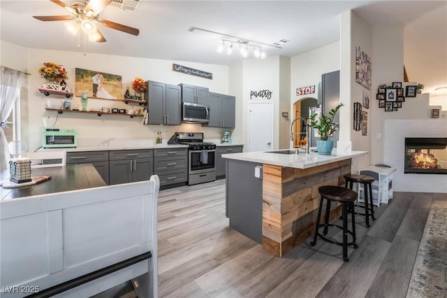 kitchen featuring a breakfast bar area, light wood finished floors, open shelves, a sink, and appliances with stainless steel finishes