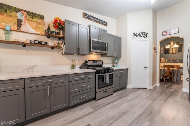 kitchen featuring gray cabinets, open shelves, arched walkways, appliances with stainless steel finishes, and light wood finished floors