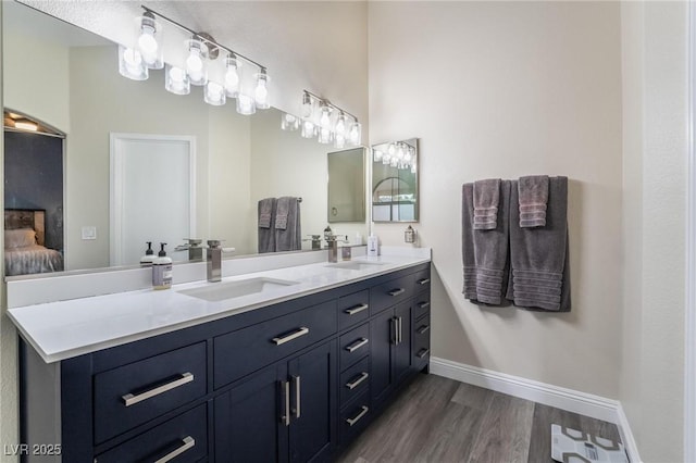 ensuite bathroom with double vanity, wood finished floors, baseboards, and a sink