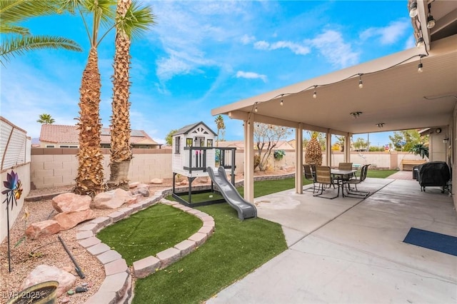 view of patio with outdoor dining space, a playground, and a fenced backyard