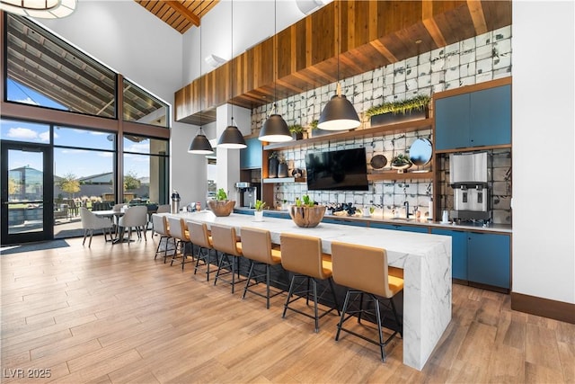 kitchen featuring light wood finished floors, a breakfast bar area, light countertops, a high ceiling, and open shelves