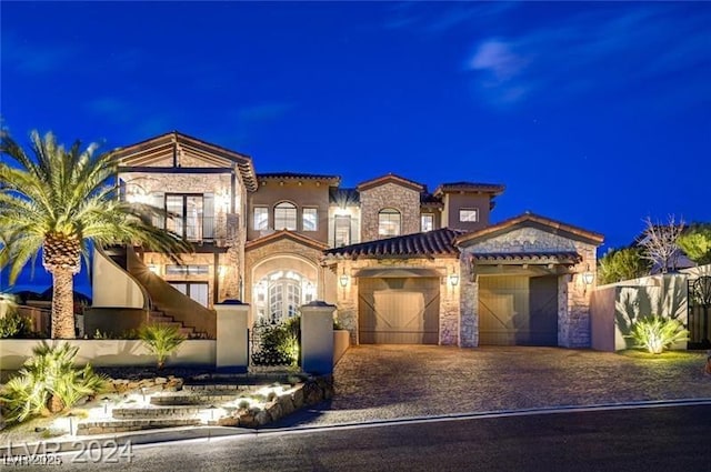 mediterranean / spanish-style home with a garage, stone siding, decorative driveway, and a tiled roof