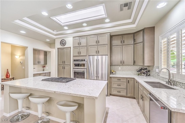 kitchen featuring a tray ceiling, a center island, a breakfast bar, stainless steel appliances, and a sink