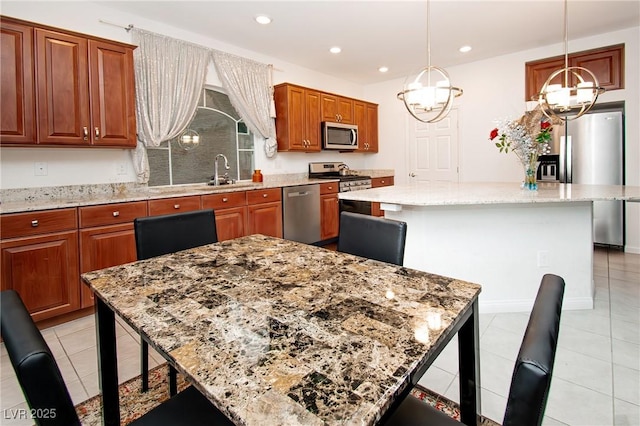 kitchen with hanging light fixtures, appliances with stainless steel finishes, a kitchen island, and light stone counters