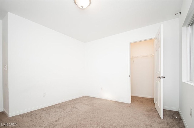 unfurnished bedroom with a closet, light colored carpet, a spacious closet, and baseboards