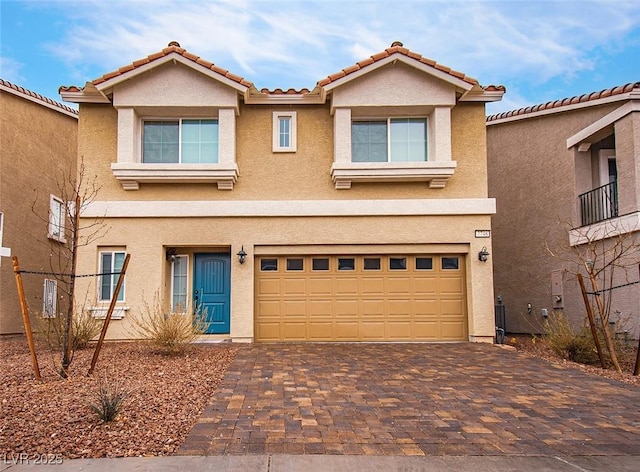 view of front of house with a garage, a tiled roof, decorative driveway, and stucco siding