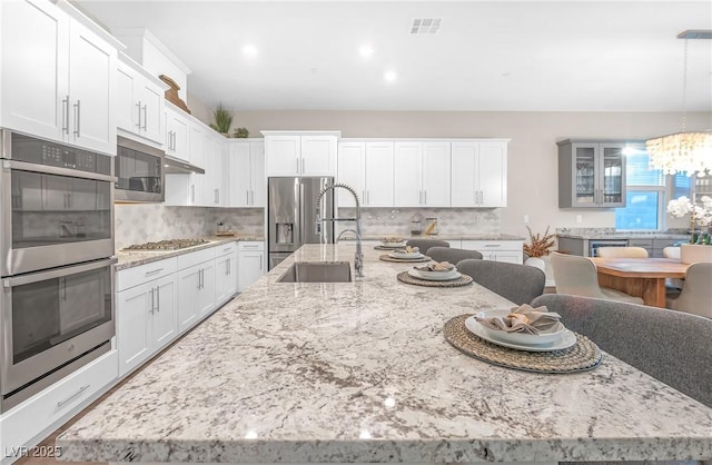 kitchen featuring white cabinets, glass insert cabinets, appliances with stainless steel finishes, decorative light fixtures, and a sink