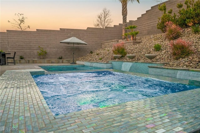 pool at dusk with a fenced backyard and a hot tub