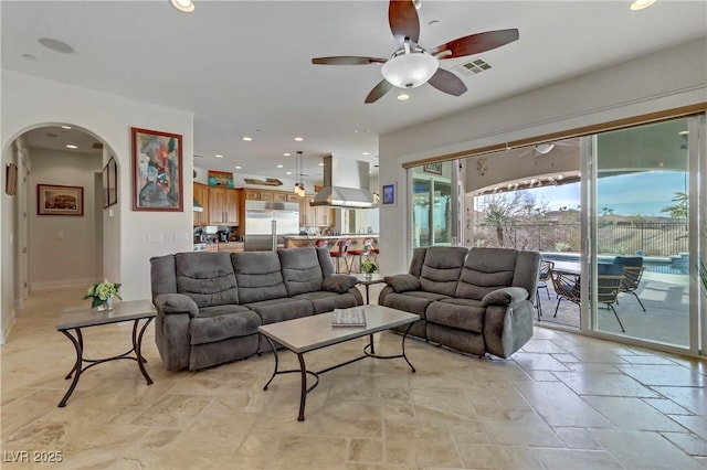 living room featuring arched walkways, recessed lighting, stone tile floors, a ceiling fan, and visible vents