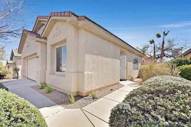 view of side of property featuring concrete driveway, a tile roof, an attached garage, and stucco siding