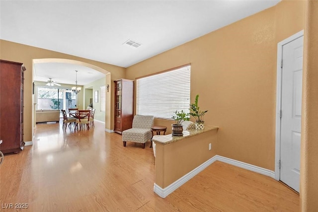 sitting room with arched walkways, light wood-style flooring, a notable chandelier, visible vents, and baseboards