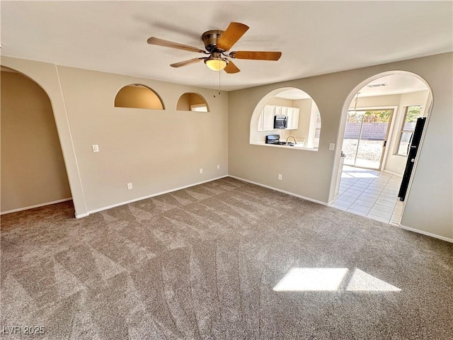 carpeted spare room with a ceiling fan, arched walkways, and baseboards