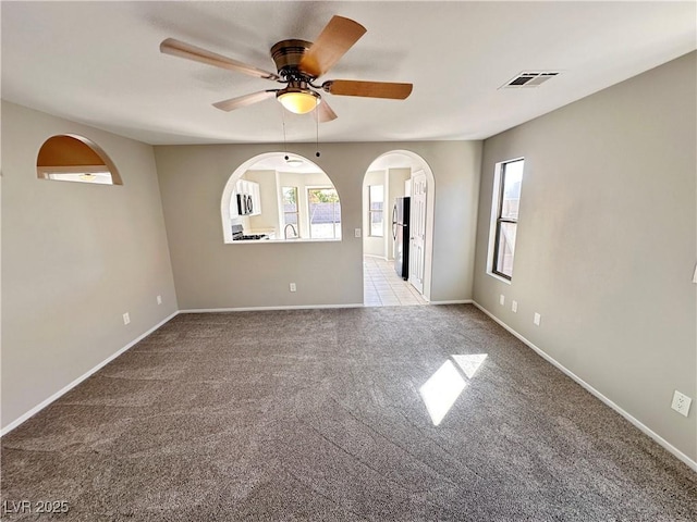 spare room featuring light colored carpet, ceiling fan, visible vents, and baseboards