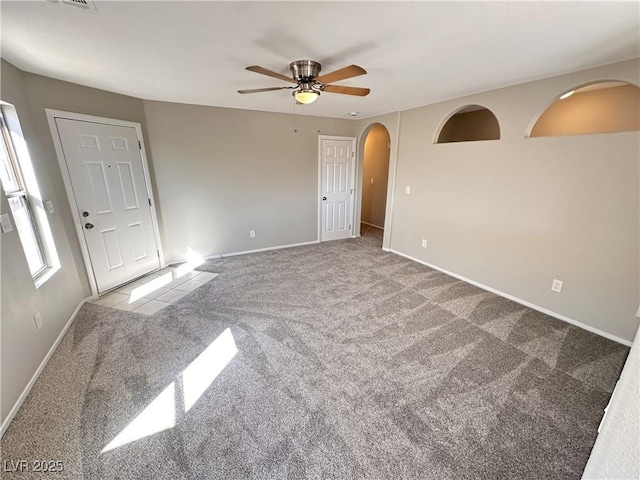 unfurnished room featuring a ceiling fan, arched walkways, light carpet, and baseboards