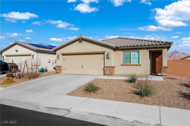 view of front of house featuring a garage, driveway, a tiled roof, roof mounted solar panels, and stucco siding