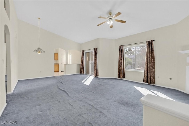 unfurnished living room featuring arched walkways, carpet floors, a ceiling fan, baseboards, and vaulted ceiling