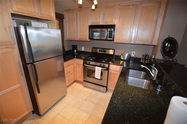 kitchen with light tile patterned floors, dark stone countertops, stainless steel appliances, light brown cabinets, and a sink