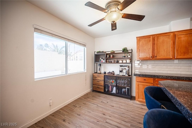 bar featuring baseboards, ceiling fan, light wood finished floors, and tasteful backsplash